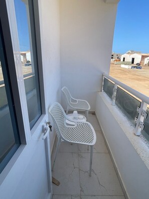 A balcony with two white metal chairs and a small table, a glass door, and a view of a parking area. - Peaceful 1-bedroom apartment with AC and fully equiped in Santa Maria (Santa Maria)