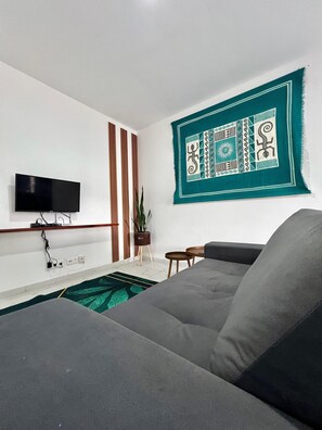 A living room with a flat-screen TV mounted on the wall, a grey sofa, a patterned rug, and a wall hanging with geometric designs. - Peaceful 1-bedroom apartment with AC and fully equiped in Santa Maria (Santa Maria)