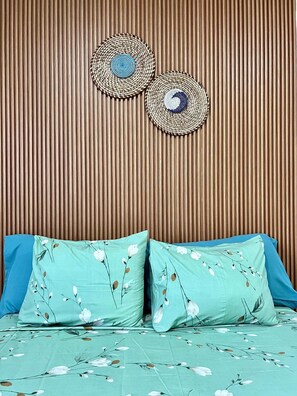 A bed with floral bedding and two pillows, a wooden slatted wall, and two woven wall hangings. - Peaceful 1-bedroom apartment with AC and fully equiped in Santa Maria (Santa Maria)