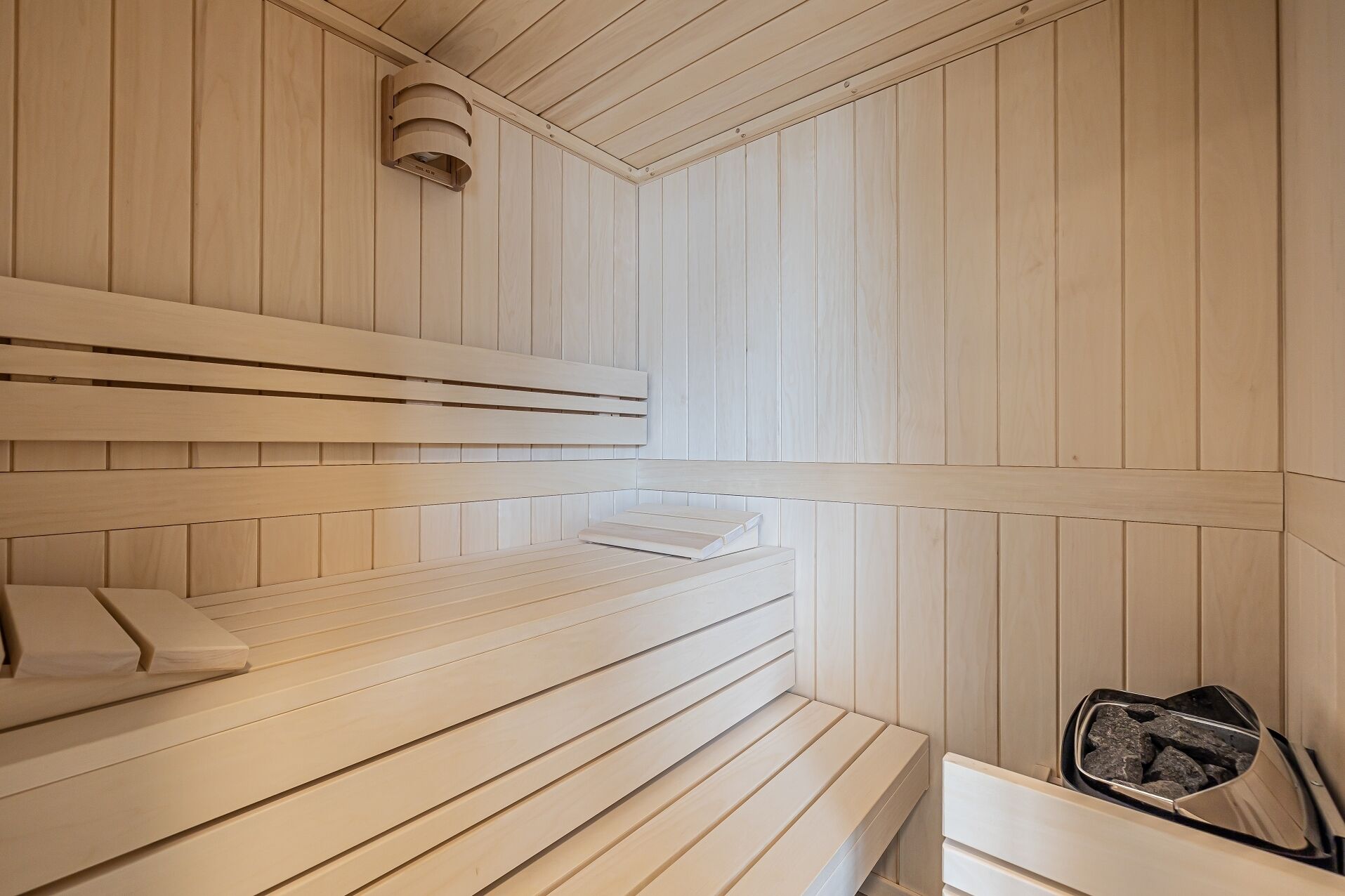 En sauna med træbænke og et lille bord, en fastmonteret varmeovn og en bakke med sten.