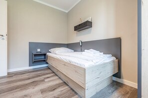 Ein Einzelbett mit Holz Kopfteil, ein Nachttisch mit Telefon und ein Regal über dem Bett.