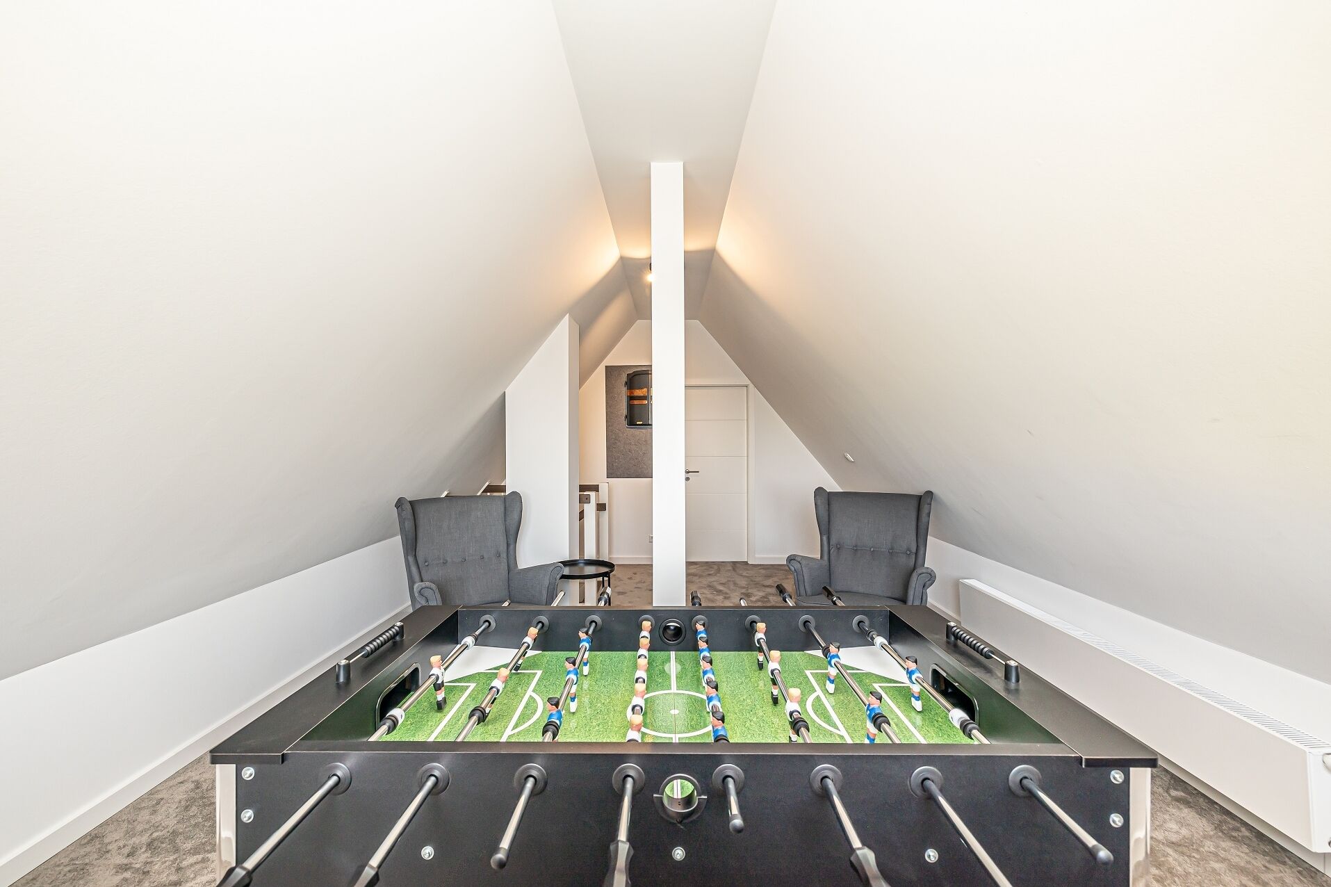 A room with a foosball table, two chairs, and a door leading to a hallway.