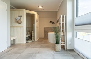 Ein modernes Badezimmer mit Dusche, Toilette und Waschbecken. Eine Pflanze in einem gewebten Korb und eine an der Wand angelehnte Leiter sind ebenfalls vorhanden.