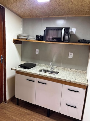 Cozinha compacta com micro-ondas, pia e bancada.