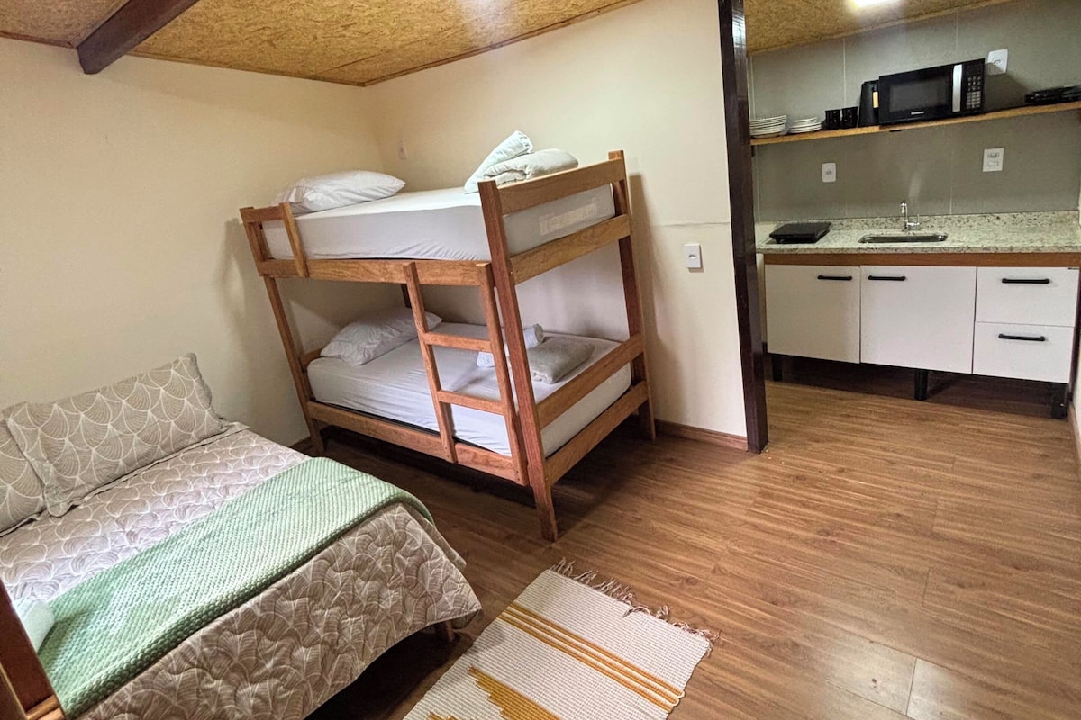 Um quarto com beliche, sofá, cozinha compacta com pia e tapete estampado.