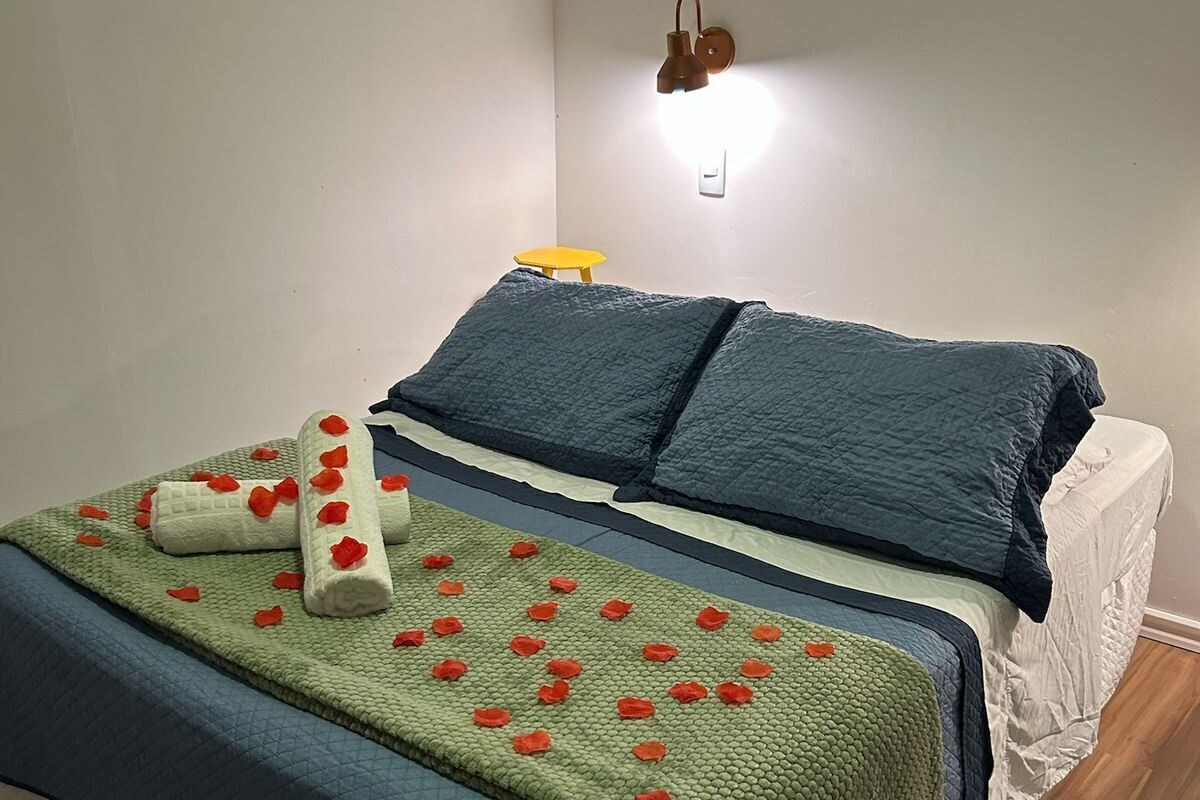 A neatly made bed with a blue and green quilt, a white mattress, and a small yellow stool against the wall.