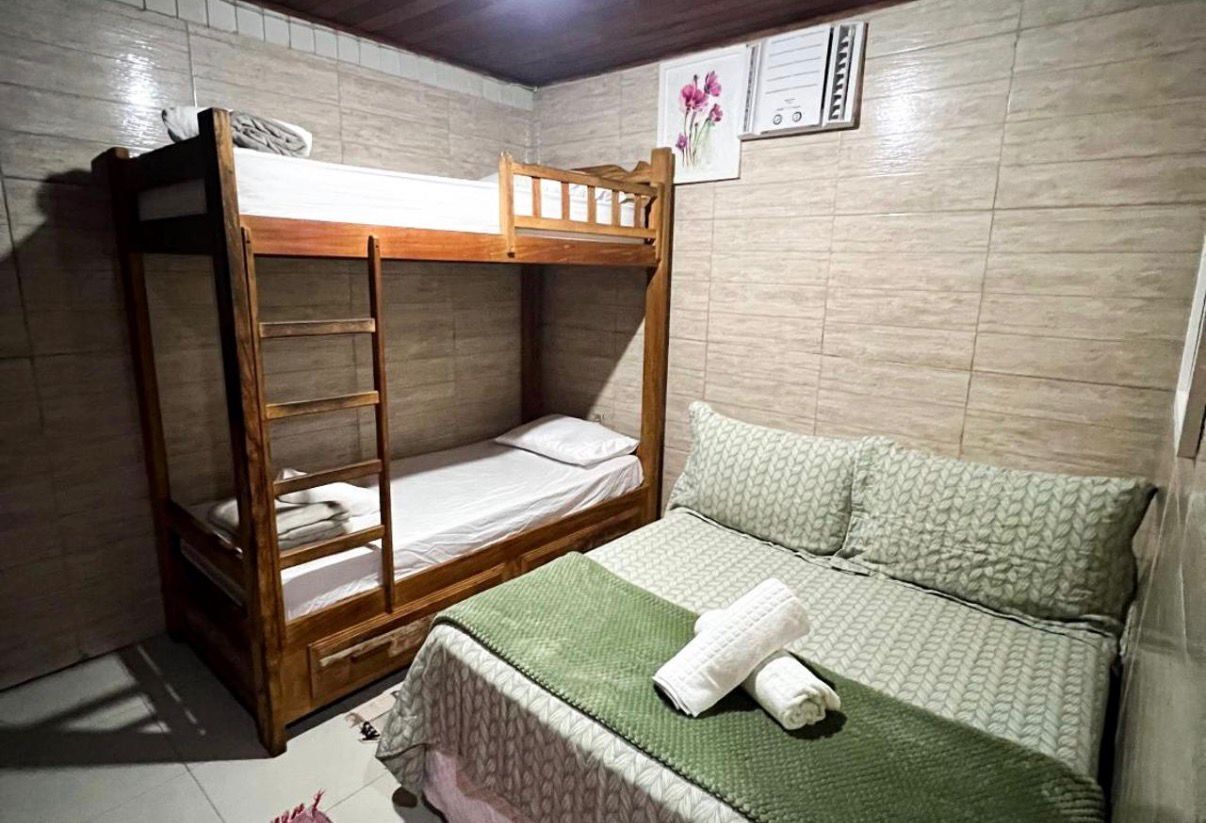 Uma cama beliche com escada, uma cama de solteiro com cobertor verde e um ar condicionado fixado na parede.