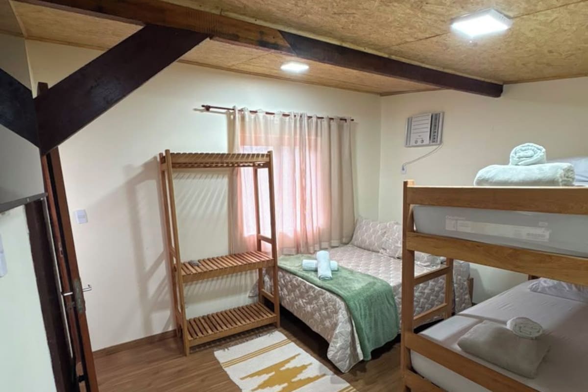 A small, cozy room with a bunk bed, a single bed, a wooden ceiling, and a window with curtains.