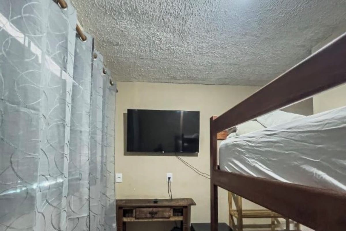 Quarto compacto com beliches, uma escrivaninha e uma televisão.