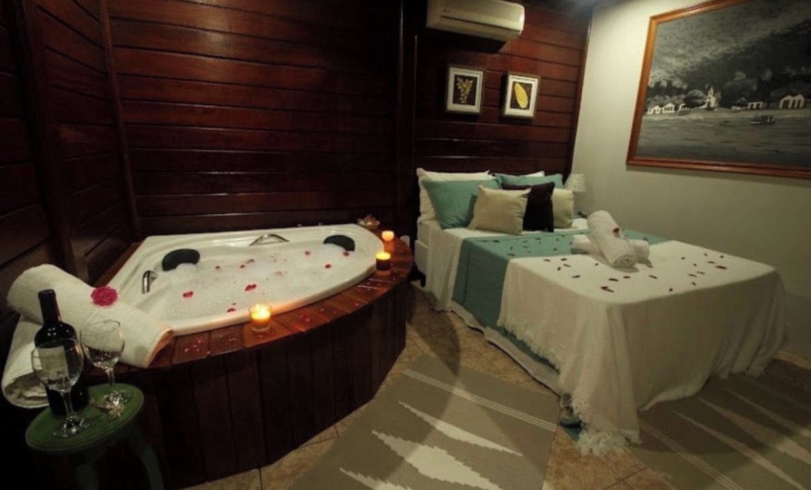 Quarto com hidromassagem, uma cama e uma mesinha com garrafa e copos.