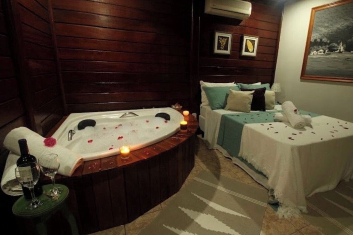 A room with a hot tub, a bed, and a small table with a bottle and glasses.