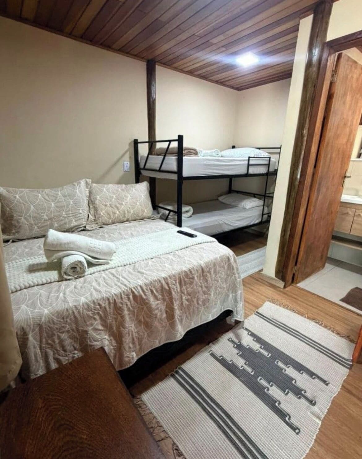 Un dormitorio con una cama litera, una cama individual y un banco de madera.