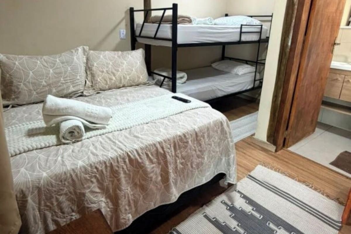 Quarto com cama de solteiro, beliche e um banco de madeira.