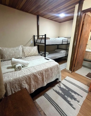Quarto com cama de solteiro, beliche e um banco de madeira.