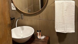 Een badkamer met een ronde spiegel, een witte wastafel, een handdoek en een houten aanrecht.