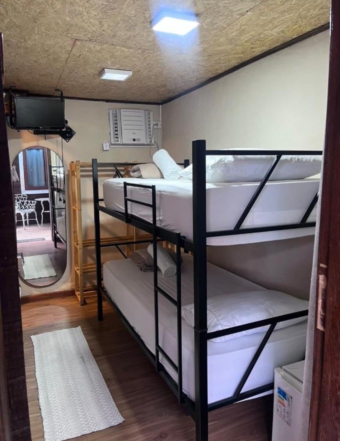 A bunk bed room with a television, a mirror, and a small kitchenette.