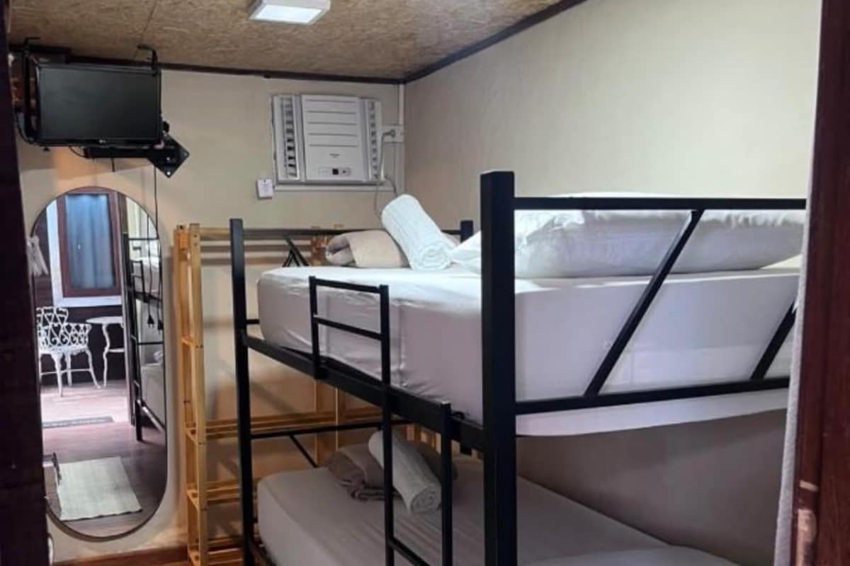 A bunk bed room with a television, a mirror, and a small kitchenette.