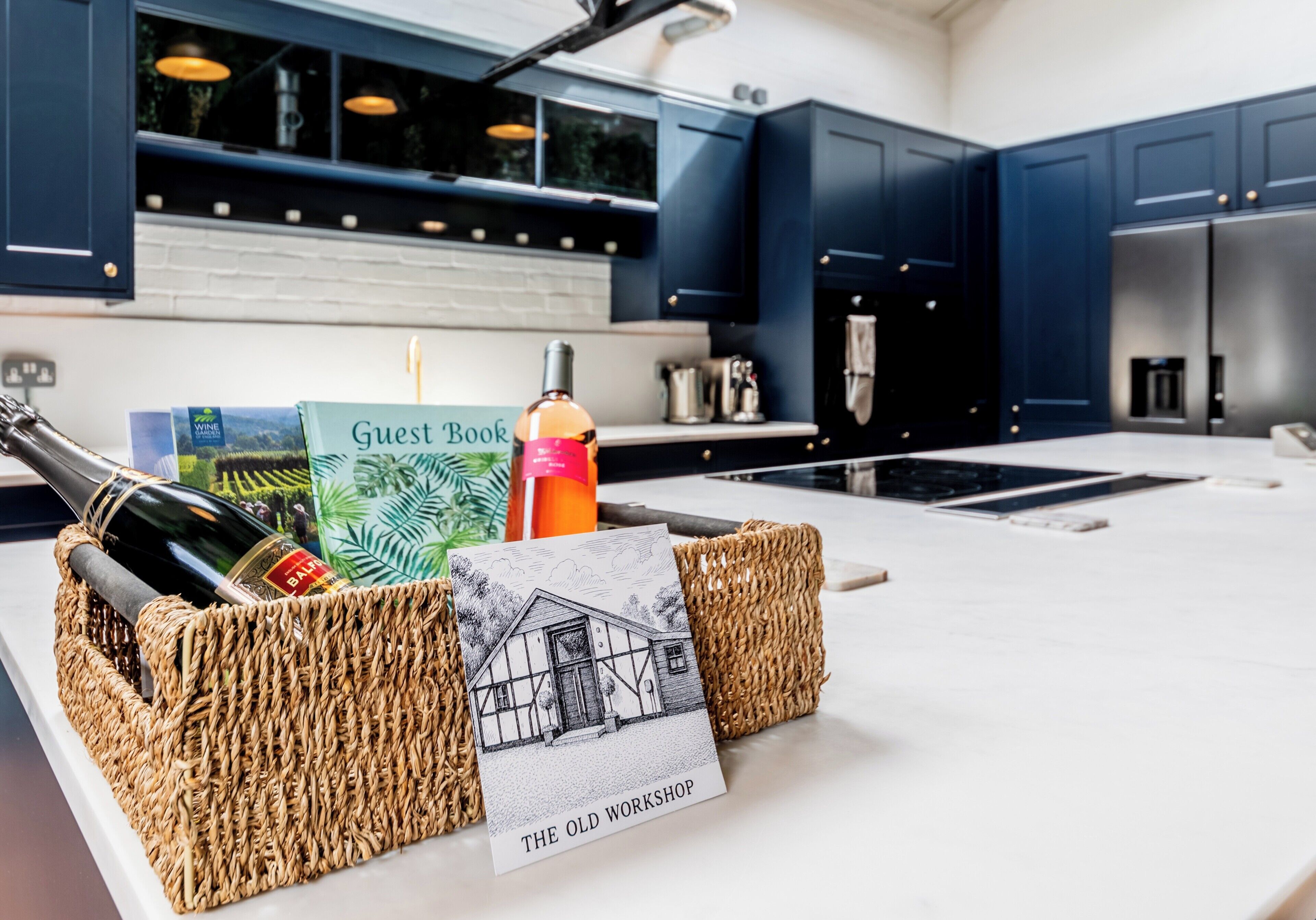 A kitchen with dark blue cabinets, a white countertop, and a woven basket holding bottles and a guest book.