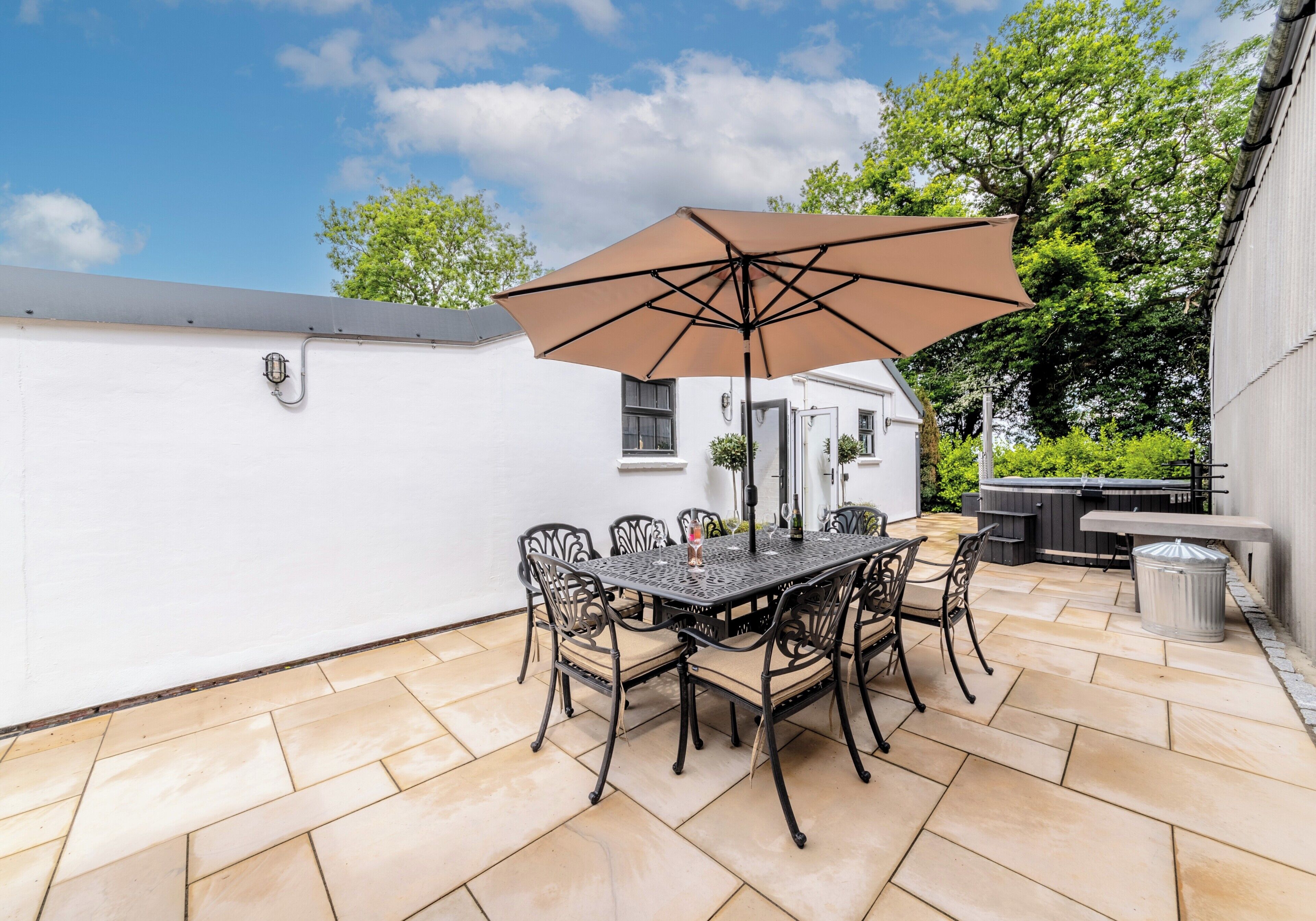 An outdoor patio with a table and chairs, a large umbrella, and a hot tub.
