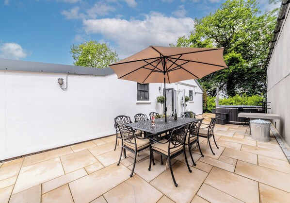 Un patio al aire libre con una mesa, sillas, una sombrilla grande y un jacuzzi.