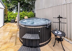 A hot tub with a wooden deck, a metal stand with a bottle, and a metal rack with glasses.
