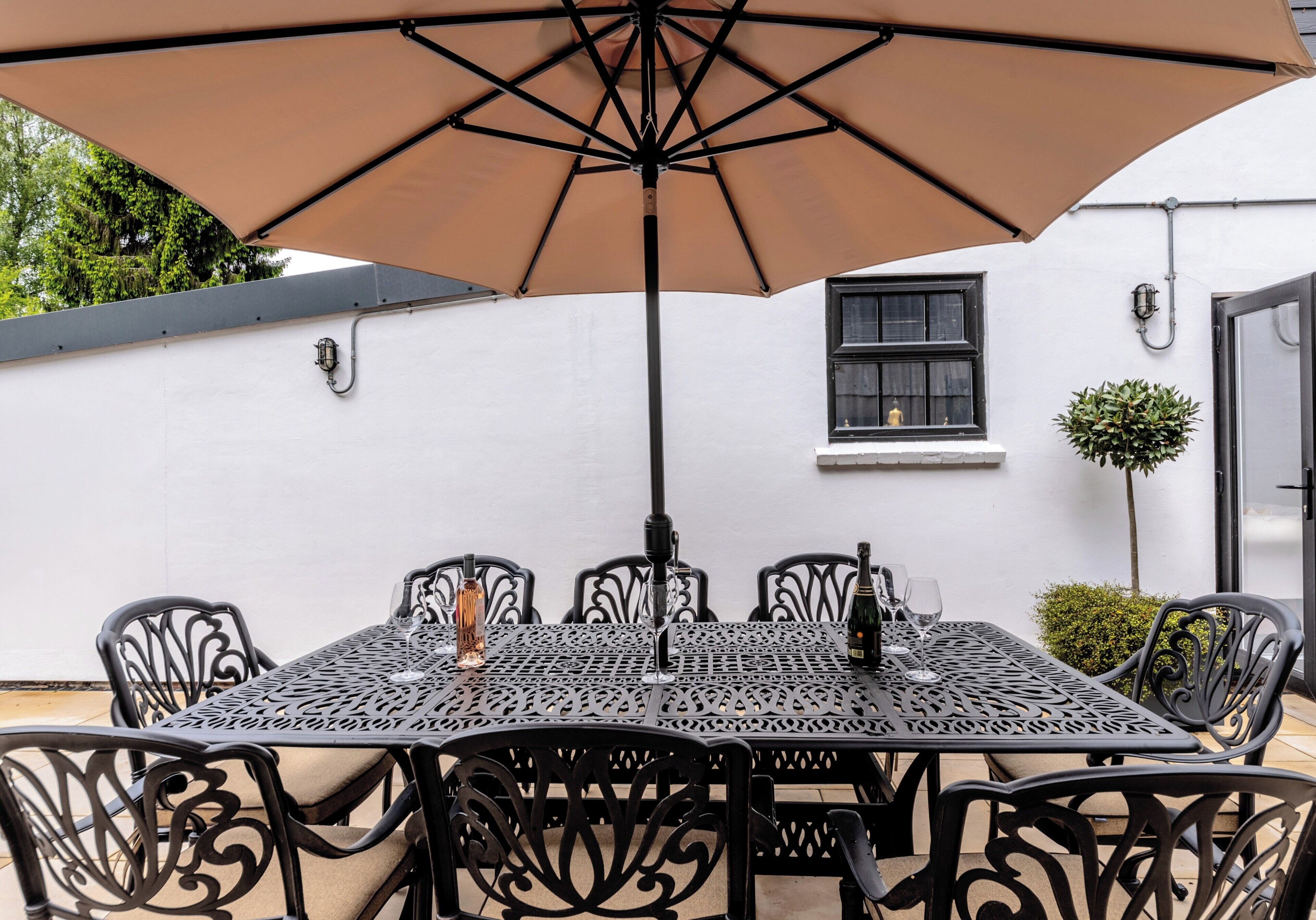 An outdoor patio with a table and chairs, an umbrella, and a white building in the background.