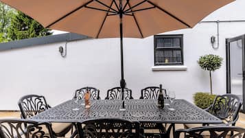 An outdoor patio with a table and chairs, an umbrella, and a white building in the background.