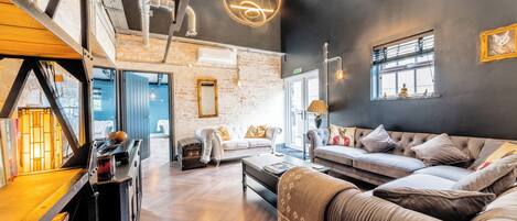 A modern interior with a loft-style ceiling, a sofa set, a fireplace, and a bookshelf.