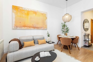 A modern living room with a grey sofa, a round coffee table, a dining area with a table and chairs, a large abstract painting, and a hanging light fixture. - A one-bedroom in the heart of Chueca, where jewel-box interiors create a quiet world of their own amid Madrid's best galleries, restaurants and nightlife. (MADRID)