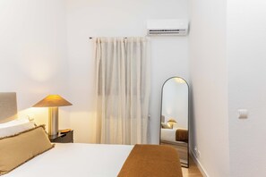 A hotel room with a bed, a nightstand, a lamp, a mirror, and an air conditioning unit. - A one-bedroom in the heart of Chueca, where jewel-box interiors create a quiet world of their own amid Madrid's best galleries, restaurants and nightlife. (MADRID)