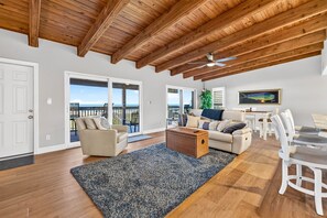 A spacious living room with a high wooden ceiling, a large window overlooking a balcony, and a dining area with white furniture. - Turtles Nest Gulf-Front Condo in Treasure Island (Treasure Island)