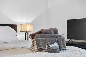 A hotel room with a bed, a chair with towels, a lamp, and a TV. - Turtles Nest Gulf-Front Condo in Treasure Island (Treasure Island)