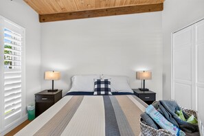 Ein Schlafzimmer mit einem Bett, zwei Nachttischen mit Lampen, einem Fenster mit Jalousien und einer Tür.