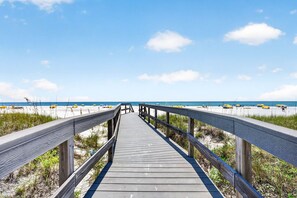 Ein Holzsteg führt zu einem Strand mit Sonnenschirmen.