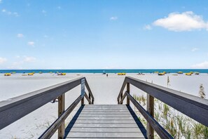A wooden boardwalk leading to a beach with umbrellas and a clear sky. - Turtles Nest Gulf-Front Condo in Treasure Island (Treasure Island)