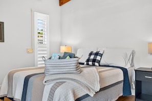 Ein ordentlich bezogenes Bett mit einer gestreiften Decke, ein Nachttisch mit einer Lampe und ein an der Wand befestigtes Regal mit Büchern.