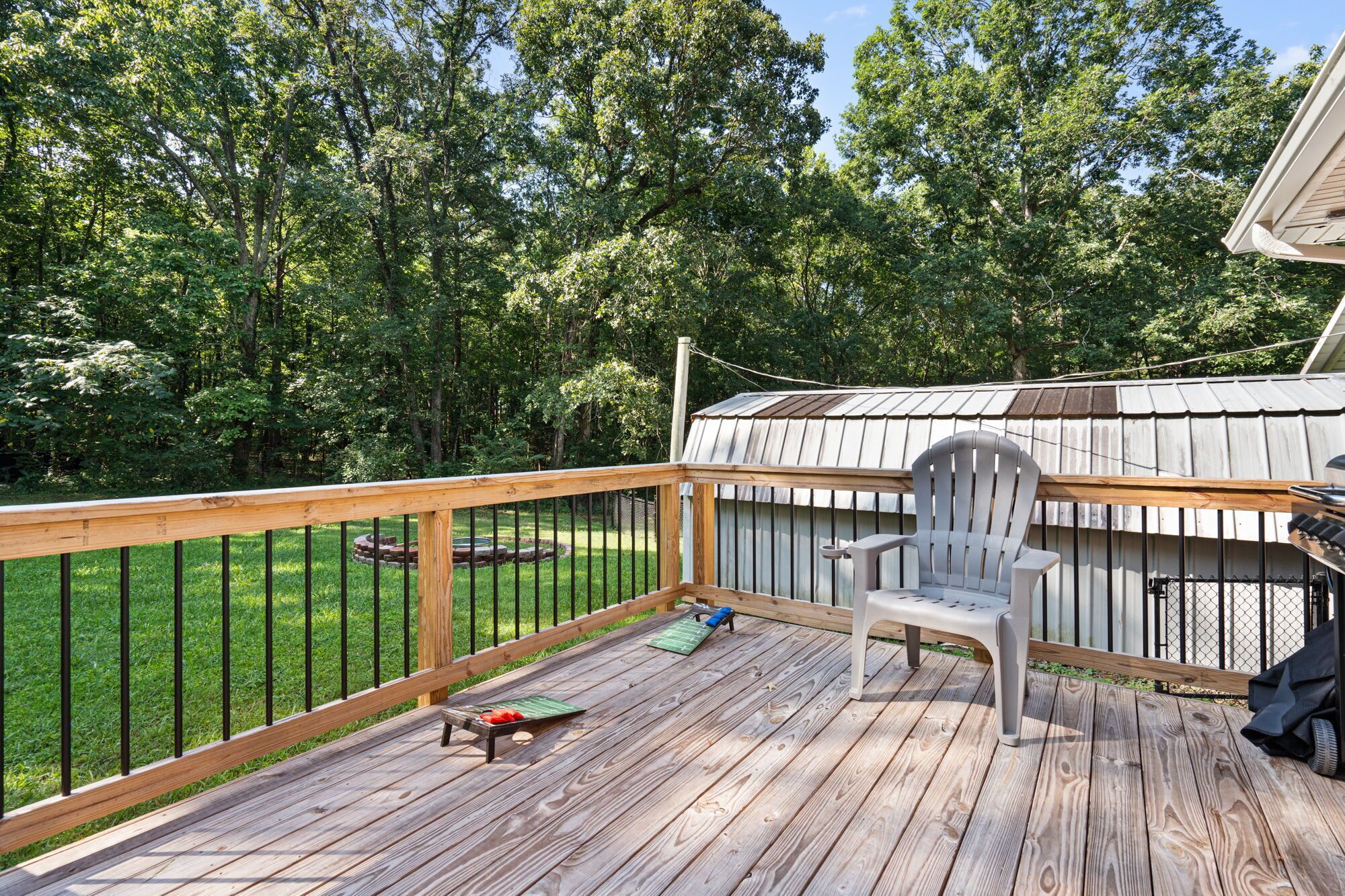 Une terrasse en bois avec une rambarde en métal, une chaise Adirondack blanche et un espace barbecue.