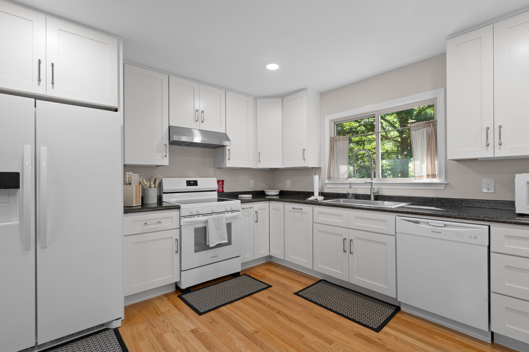A modern kitchen with white cabinetry, a stainless steel range hood, a built-in oven, and a dishwasher.