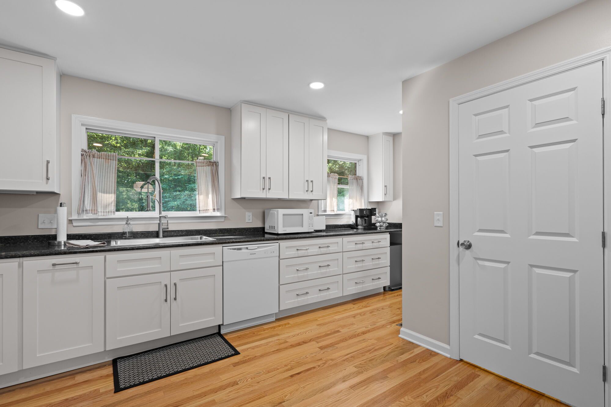 A modern kitchen with white cabinets, a black countertop, and a wooden floor.