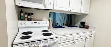A compact kitchen with a white stove, microwave, and cabinets.