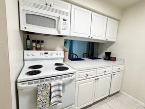 Una cocina compacta con estufa blanca, microondas y armarios.