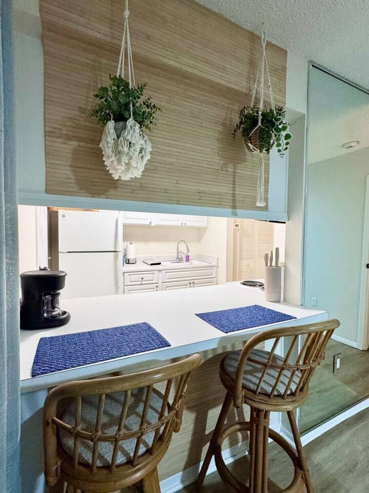 A modern kitchen with a white countertop, two wicker chairs, and hanging plants.