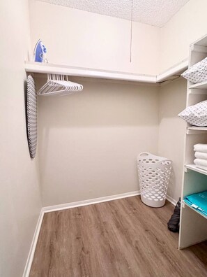 A corner closet with a hanging rack, a laundry basket, and shelves with folded towels. - Boho Coastal Studio • Near Siesta Key • Pool (Sarasota)