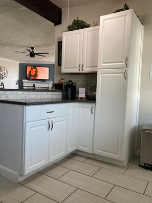 A kitchen with white cabinets, a black countertop, a ceiling fan, and a television on the left.