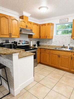 A kitchen with wooden cabinets, a granite countertop, a stainless steel sink, and a window with a view of greenery. - Spacious 4-bedroom house in tranquil Tampa with AC (Tampa)