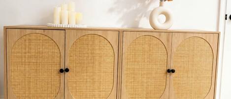 A wooden cabinet with circular woven doors, a vase with dried flowers, and candles on top.
