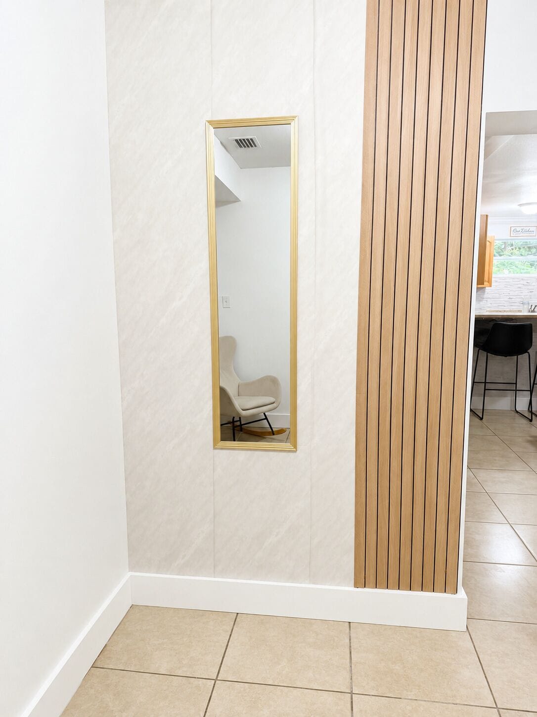 Ein Zimmer mit weißer Wand, einem Spiegel mit goldener Rahmung und einer Holzvertäfelung.