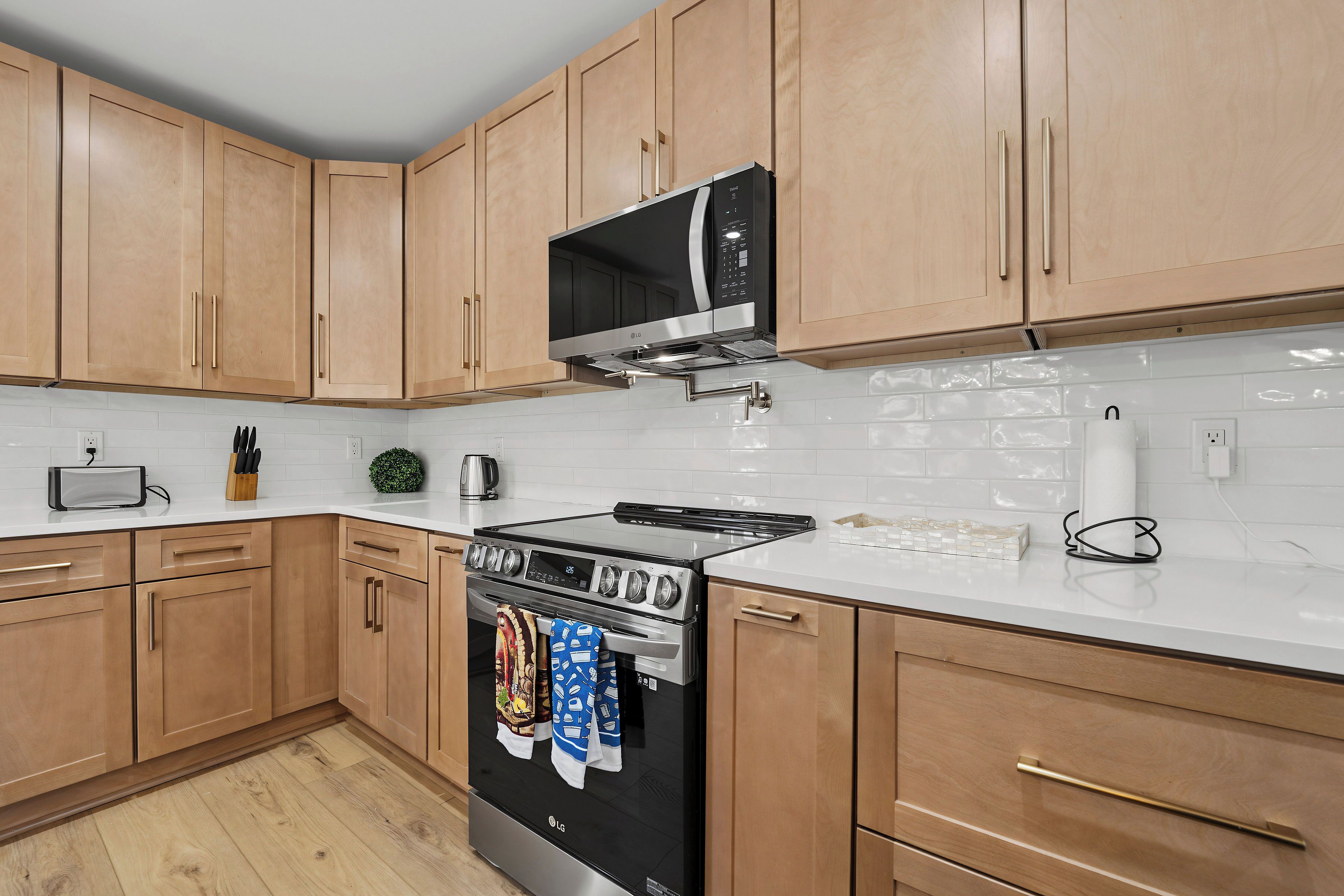 Une cuisine avec des meubles de rangement en bois, une cuisinière en acier inoxydable et un four à micro-ondes placé au-dessus.