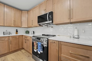 Une cuisine avec des meubles de rangement en bois, une cuisinière en acier inoxydable et un four à micro-ondes placé au-dessus.