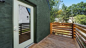 A wooden deck with a metal gate, a white door with a window, and a brick wall.